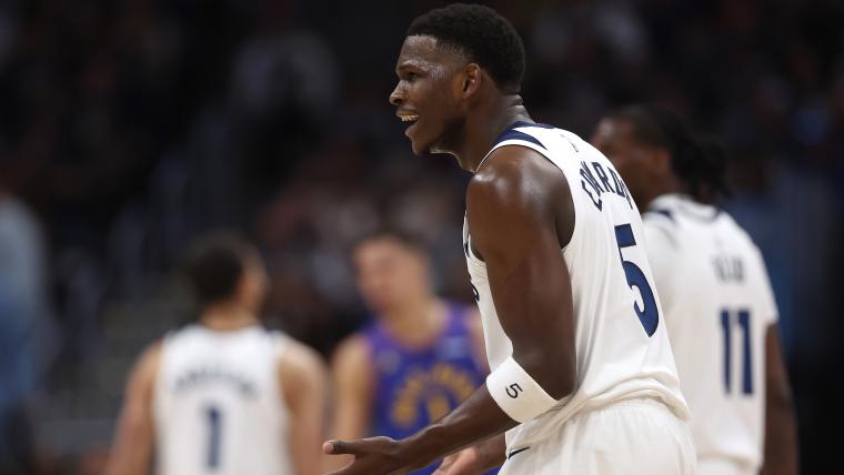 A Minnesota Timberwolves player wearing the number 5 jersey appears animated and expressive during a game, possibly reacting to a call or play. Teammates are partially visible in the background.
