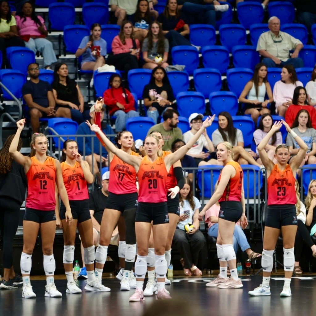 A volleyball team in colorful jerseys celebrates or reacts during a match, with players raising their arms and fans in the background.