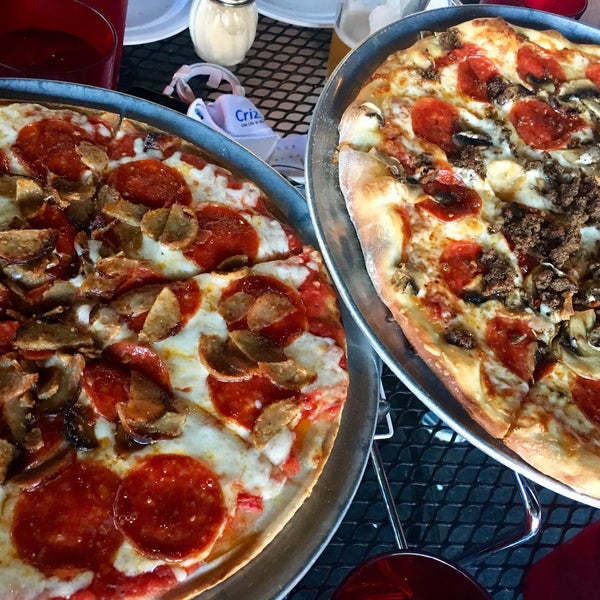 Two large pizzas on metal trays; one topped with pepperoni and sausage, the other with pepperoni, ground beef, and mushrooms.