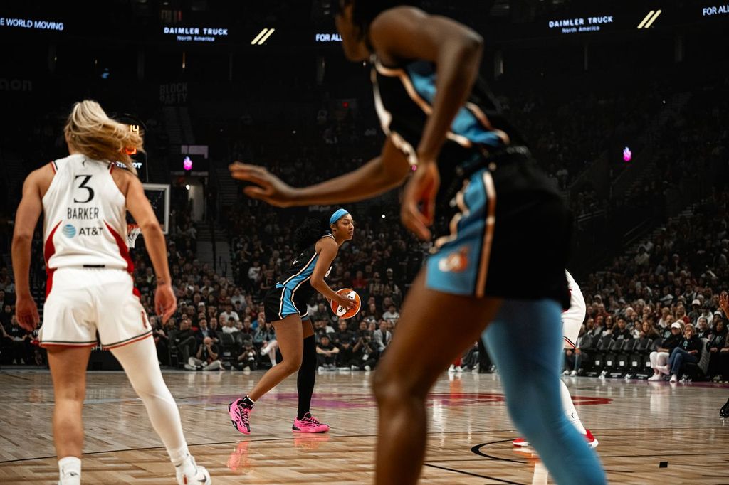 A basketball player in a blue uniform prepares to pass the ball during a game, with another player in a white uniform visible in the foreground.