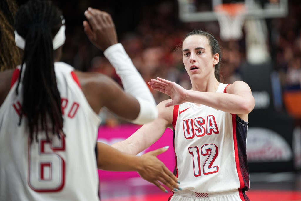 Two female basketball players are exchanging a high five on the court, with one wearing a white jersey marked 'USA 12' and the other in a red jersey labeled '6'.