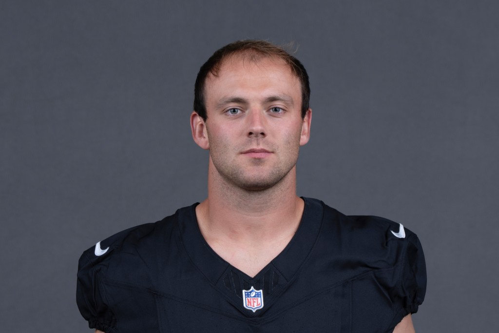 Headshot of a male football player wearing a black jersey with an NFL logo, posing against a gray background.