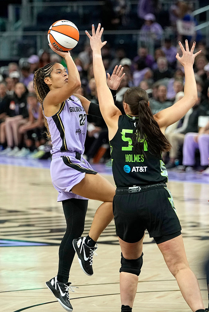 A female basketball player from the Golden State team is attempting a shot over a defender during a game, showcasing action and competitive spirit.