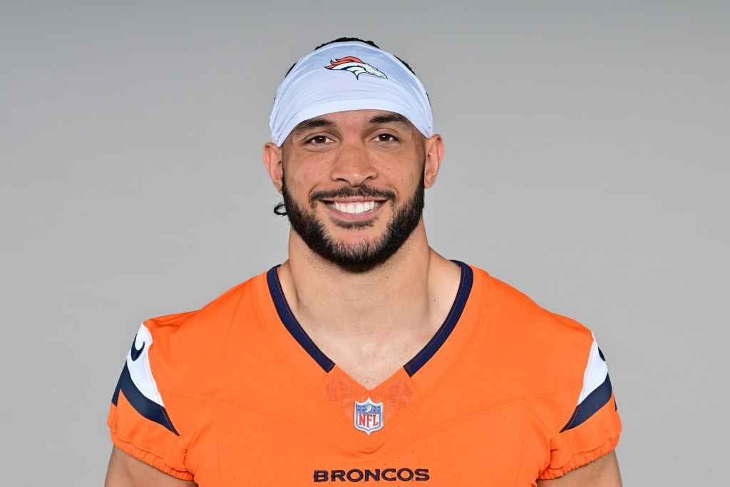 Professional football player wearing an orange NFL jersey with 'Broncos' on the front, smiling against a neutral background.