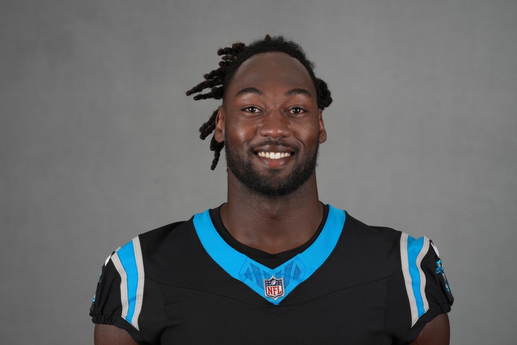 Portrait of a smiling male football player wearing a black uniform with teal accents, set against a neutral background.