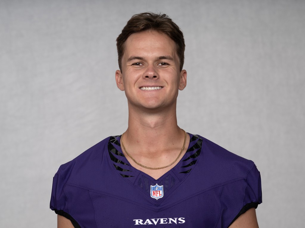 Close-up portrait of a young male football player wearing a purple NFL jersey, smiling against a neutral background.