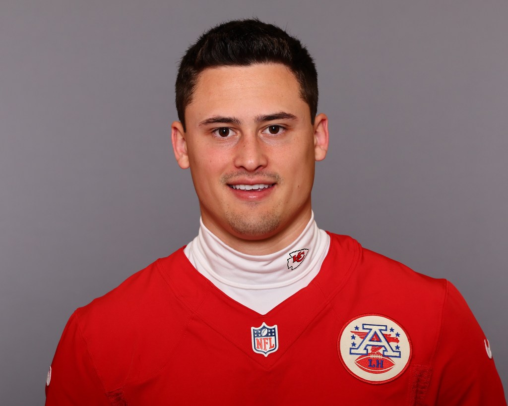 Portrait of a young male football player wearing a red jersey with an NFL logo and a white collar, smiling at the camera.