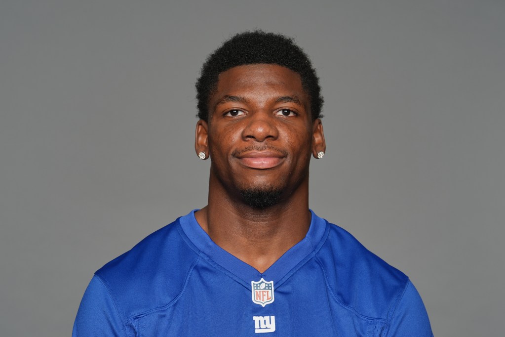 Headshot of a young man wearing a blue NFL jersey with the New York Giants logo, smiling against a neutral gray background.