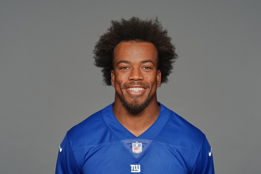 A smiling man in a blue football jersey with the NFL logo, posing against a gray background.