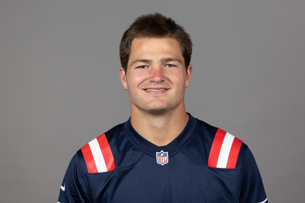 Smiling young man wearing a dark blue sports jersey with red and white stripes, posed against a neutral gray background.