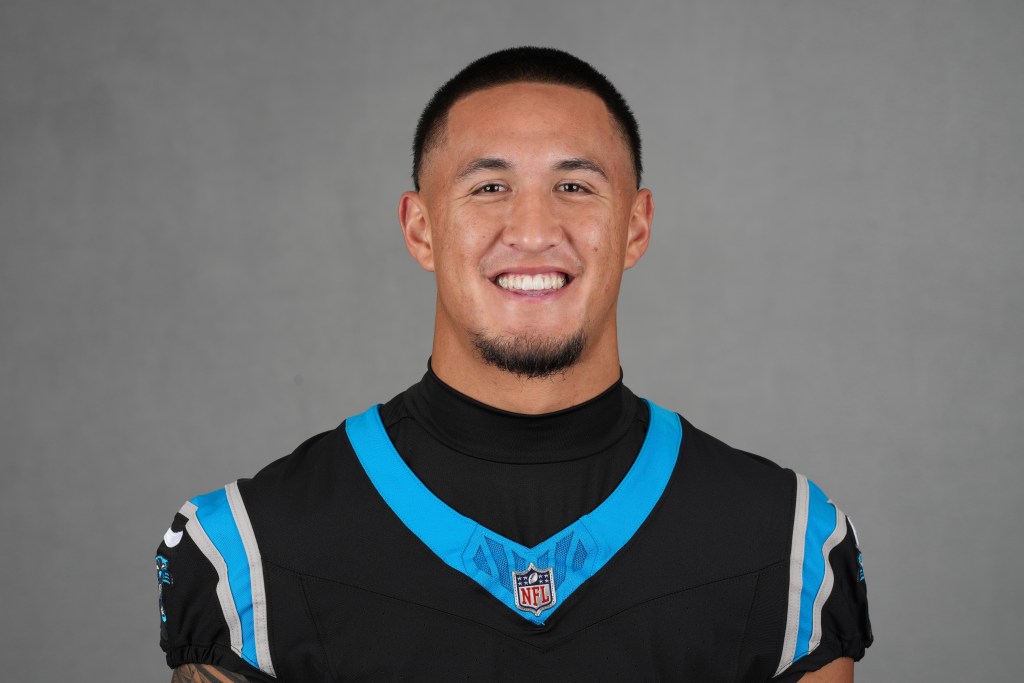 A headshot of a male football player smiling, wearing a black and blue NFL jersey with the Carolina Panthers logo.