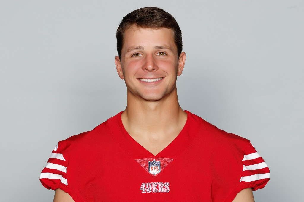 Smiling male football player wearing a red jersey with the NFL logo and the number of the team visible, against a light gray background.