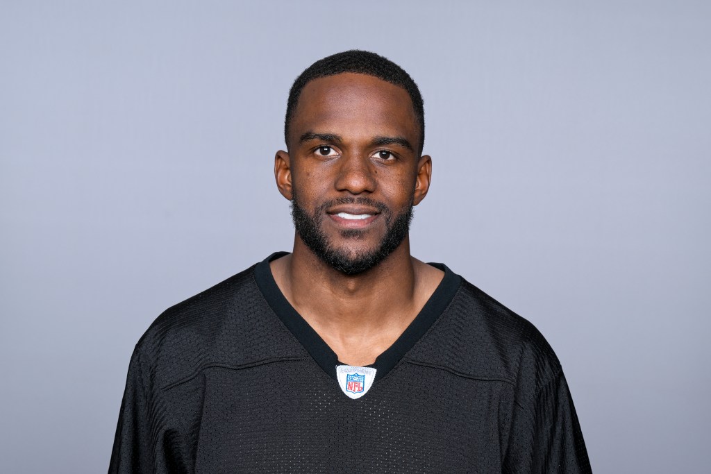 A man posing for a portrait in a black football jersey with an NFL logo, set against a neutral gray background.