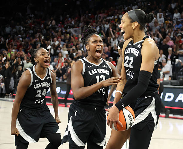 Three excited female basketball players celebrating a victory on the court, wearing black uniforms with 'Las Vegas' branding.
